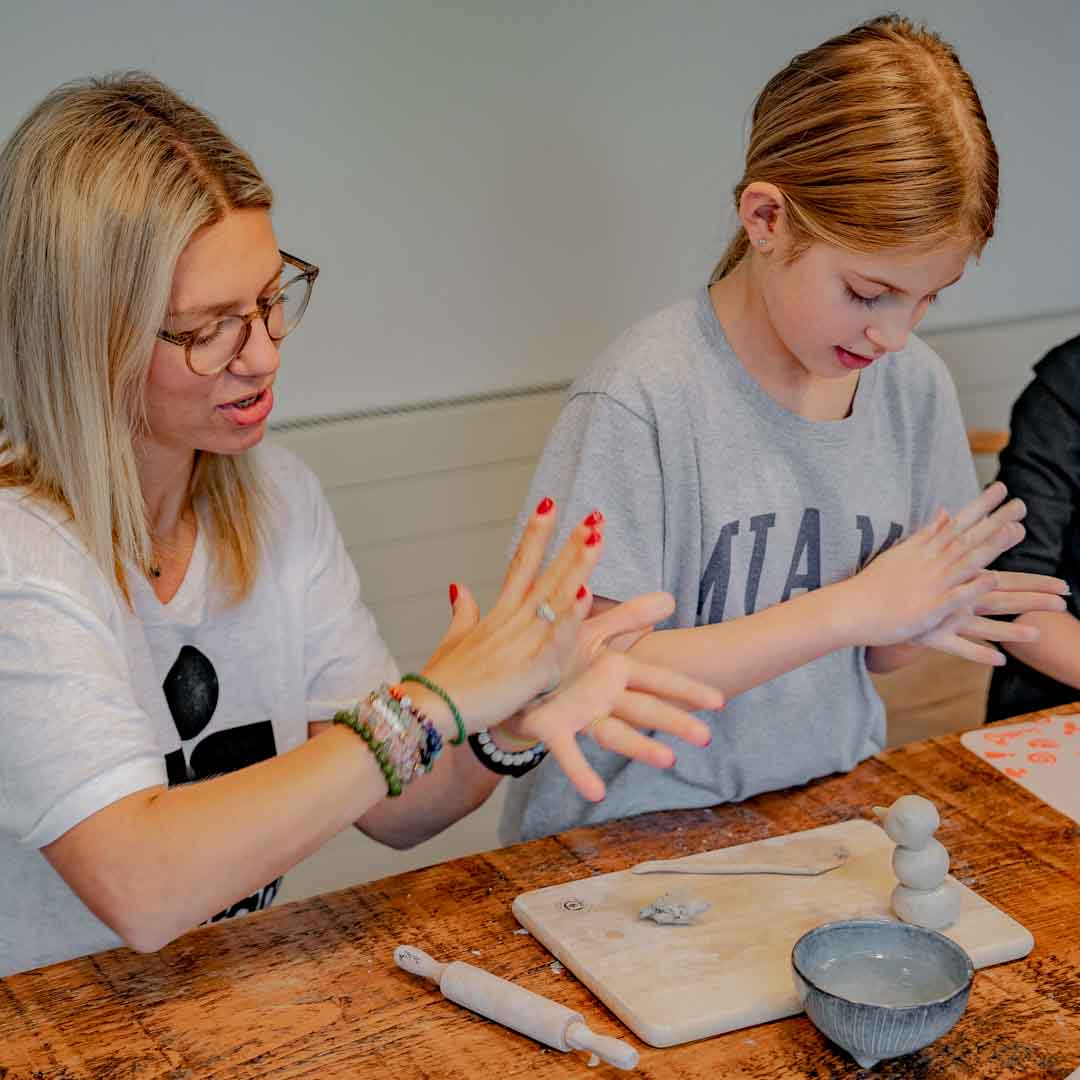 A child and her mom doing pottery together at the kitchen table