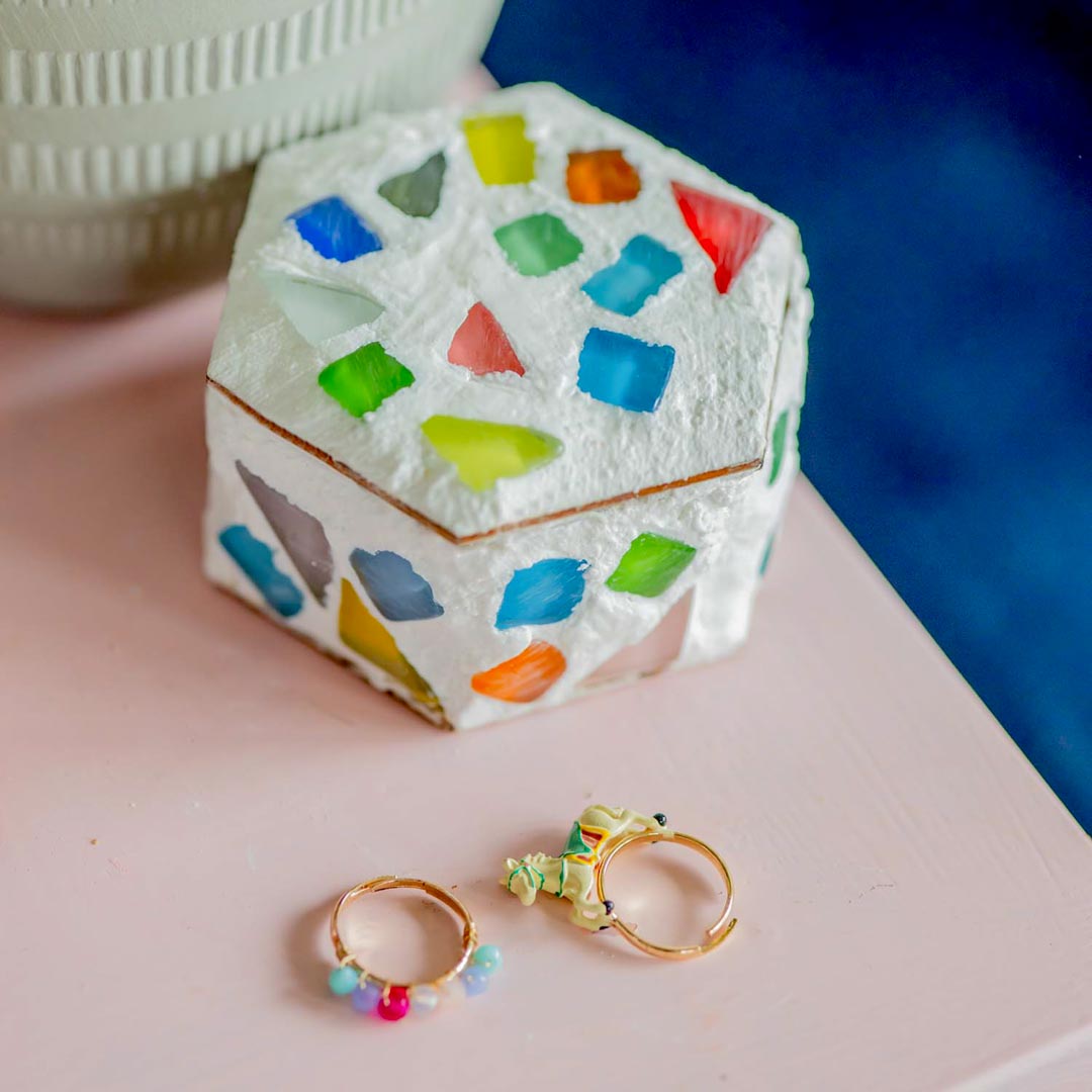 A Sculpd Kids Mosaic Kit trinket pot on a table with two rings in front of it