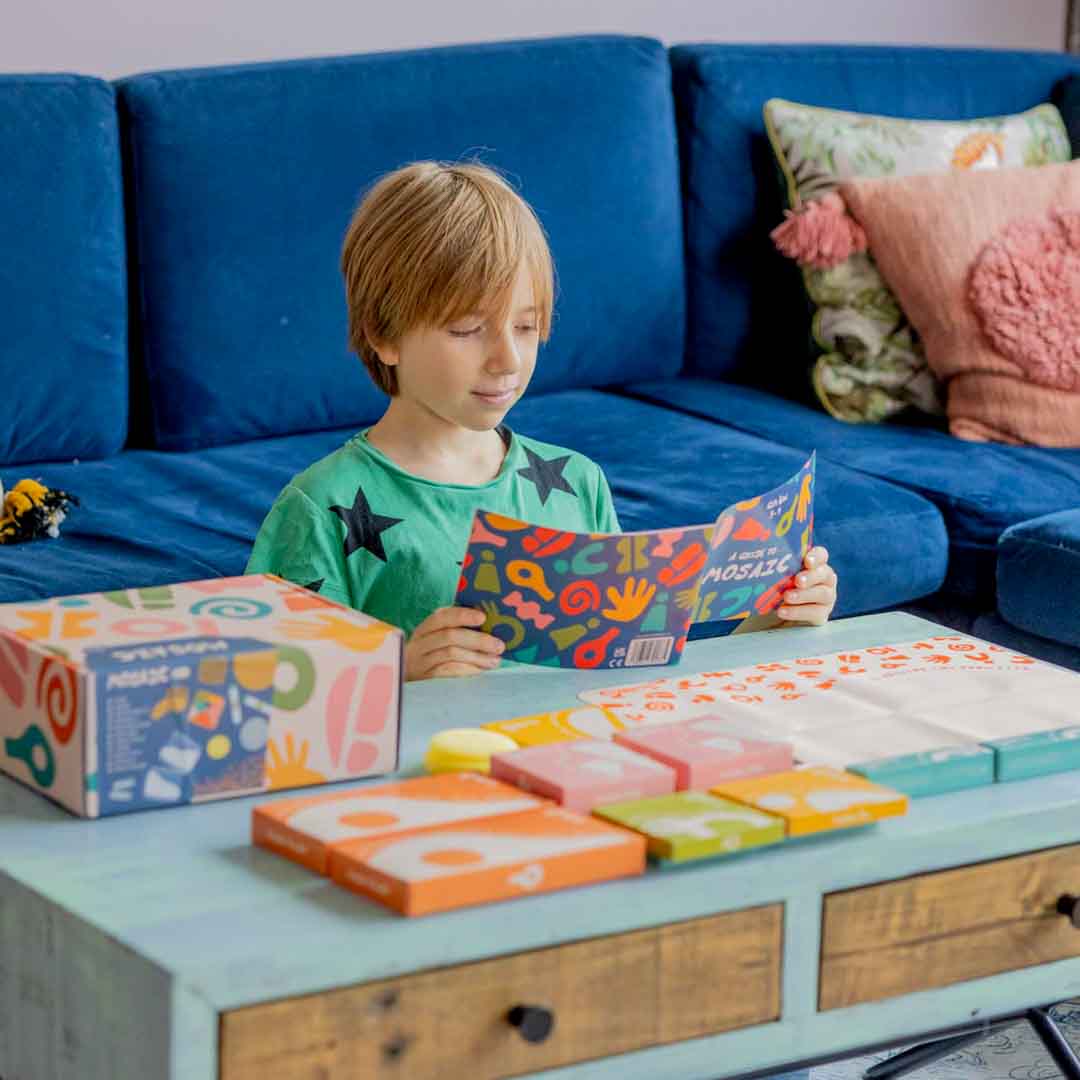 Boy in front of a coffee table holding open and reading a Sculpd Mosaic Kit guide