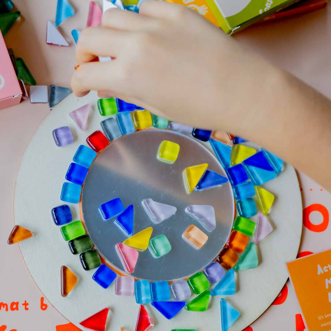 A Sculpd Kids Mosaic Kit Mirror being built by a child's hand on a table