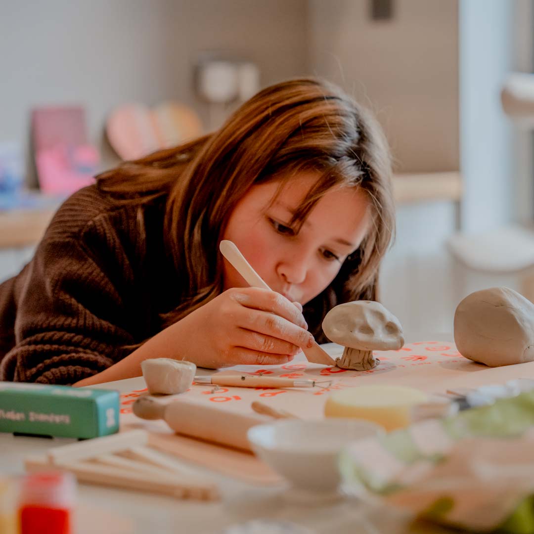 Girl with a pottery tool creating a clay mushroom on the table