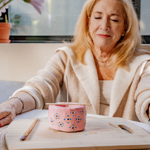 A woman relaxes with a hand-painted pink clay candle vessel in front of her made of Sculpd Candle Making Kit for Sculpd Mothers Day Candle Making Bundle