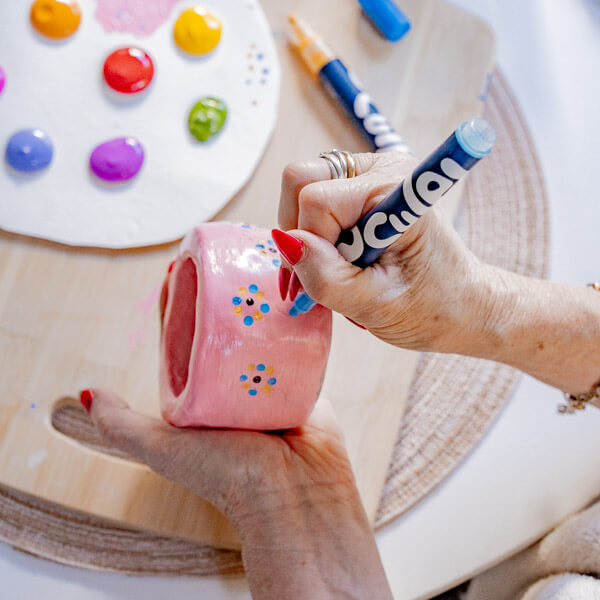 Woman paints a clay piece with Sculpd Paint Pens and tools from Sculpd Pottery Kit