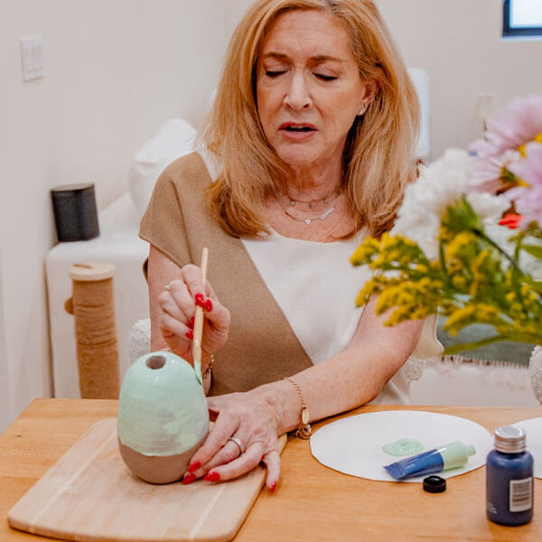 Woman paints a clay piece with Sculpd Acrylic Paint Set and tools from Sculpd Pottery Kit