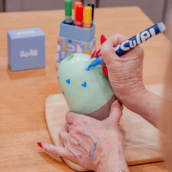 Woman paints a clay piece with Sculpd Paint Pens and tools from Sculpd Pottery Kit