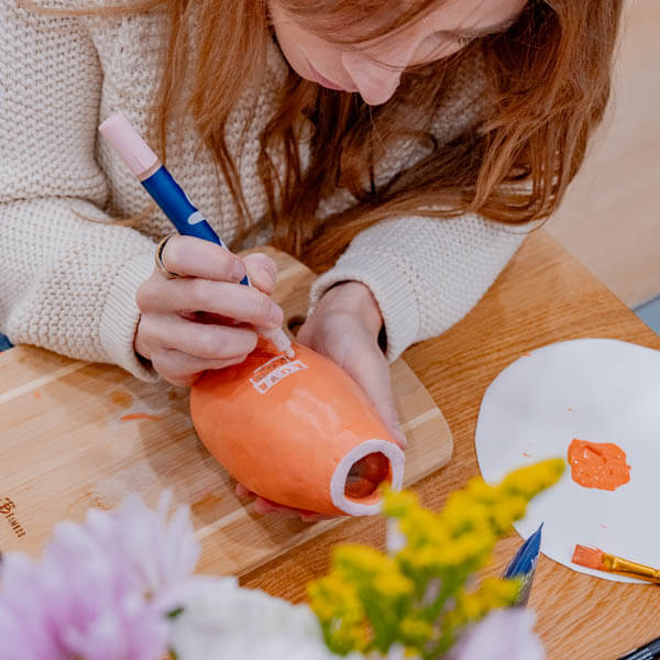 Woman paints a clay piece with Sculpd Paint Pens and tools from Sculpd Pottery Kit