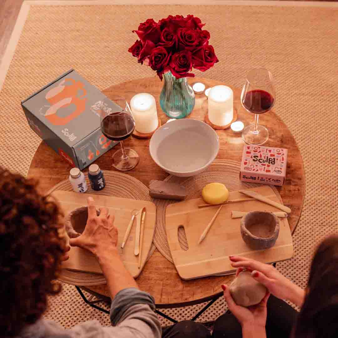 Sculpd Pottery Kit laid out on a table with roses, candles and red wine glasses with two people hand-crafting using Sculpd Air-Dry clay