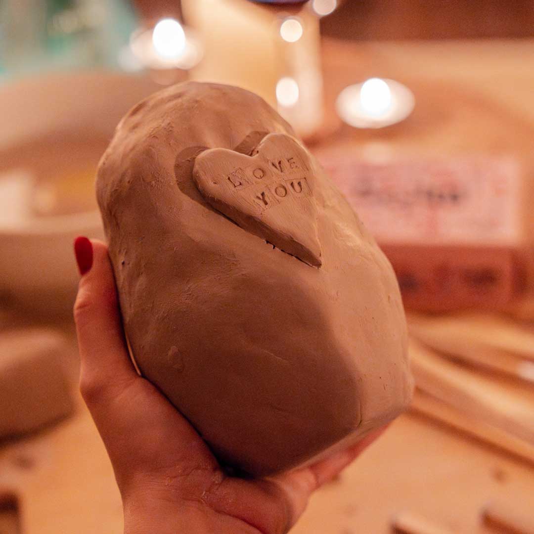 Hand holding an unpainted Sculpd Pottery vase with a heart and stamped letters saying 'Love You'