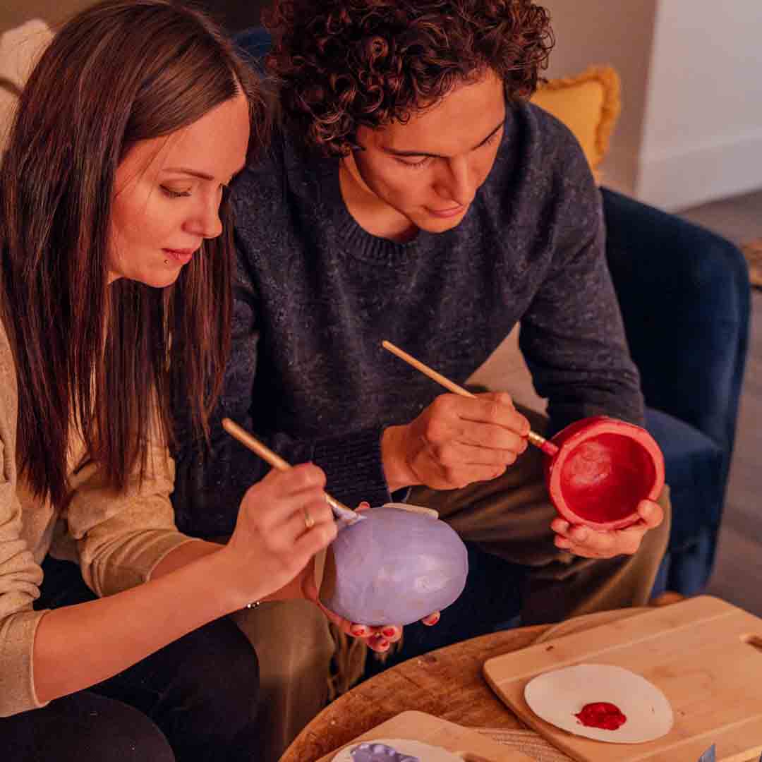 Two Sculpd Pottery clay pots being hand-painted by two people