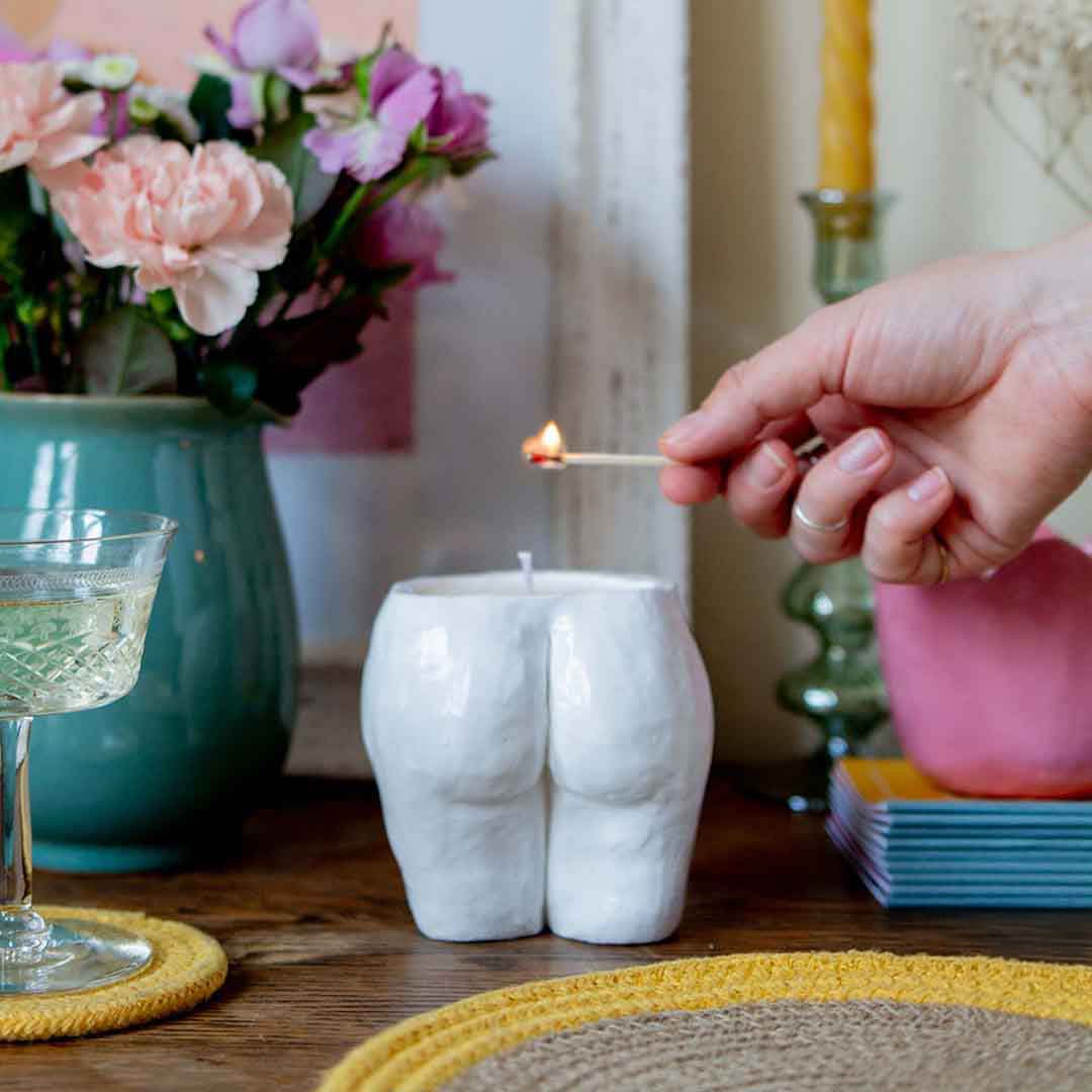 Sculpd Candle Making Kit pot being lit with a match and a stylized background with flowers