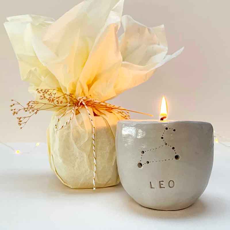 A handmade clay candle holder with a "Leo" zodiac constellation design, next to a gift wrapped in tissue paper and twine made with Sculpd Candle Making Kit