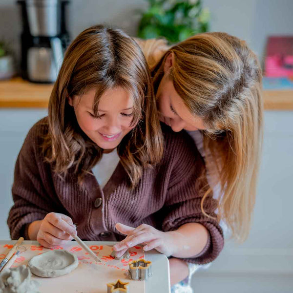 A child doing pottery at the kitchen table being watched by her mom