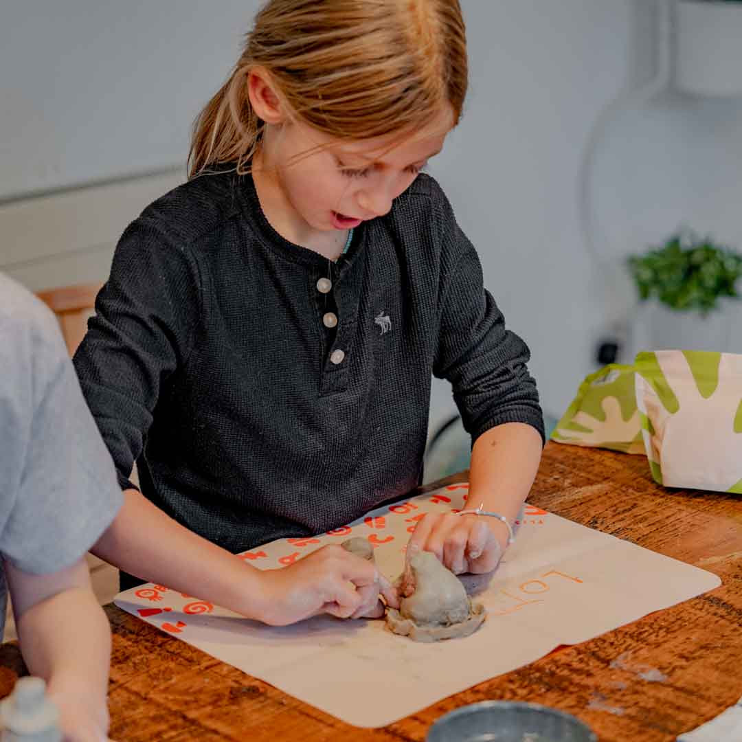 Girl hand-shaping a clay creation on a silicon mat on a table
