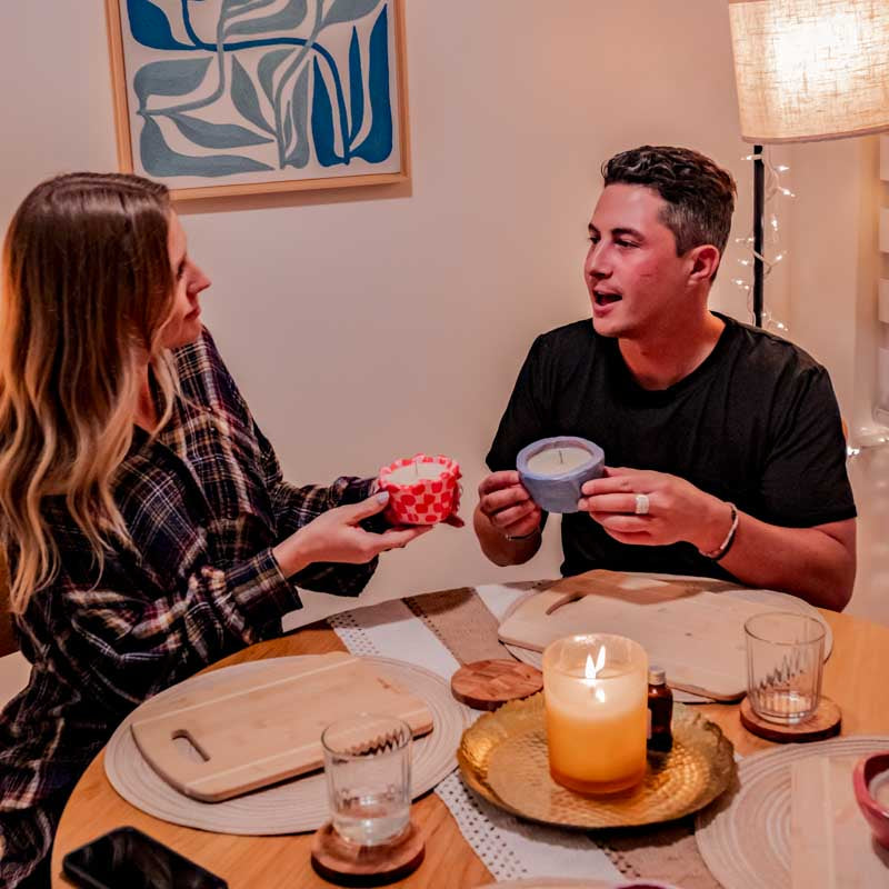 Two people holding Sculpd Candle Making Kits pots with a stylized table on the forefront