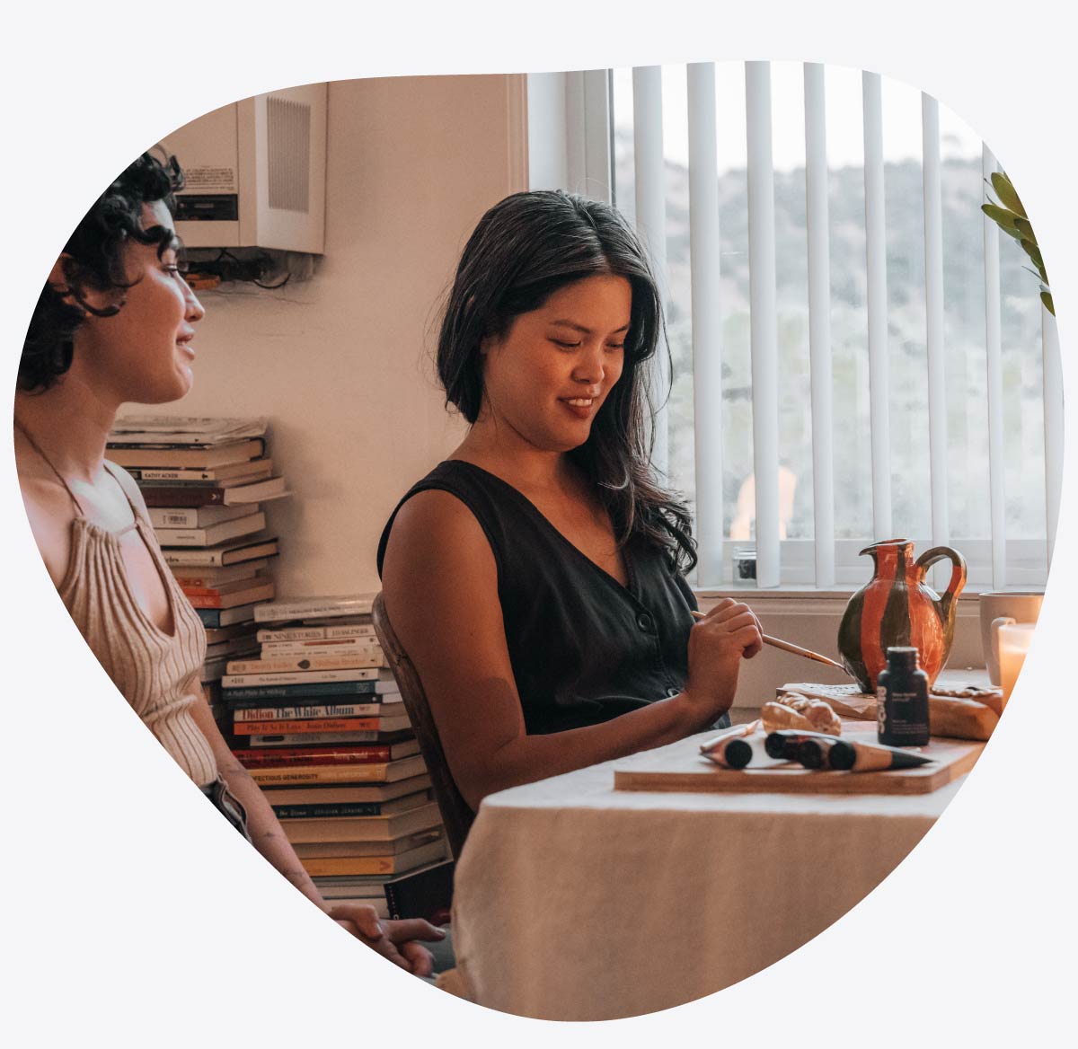Two women with the Sculpd Pottery Kit on a stylized table and books in the background