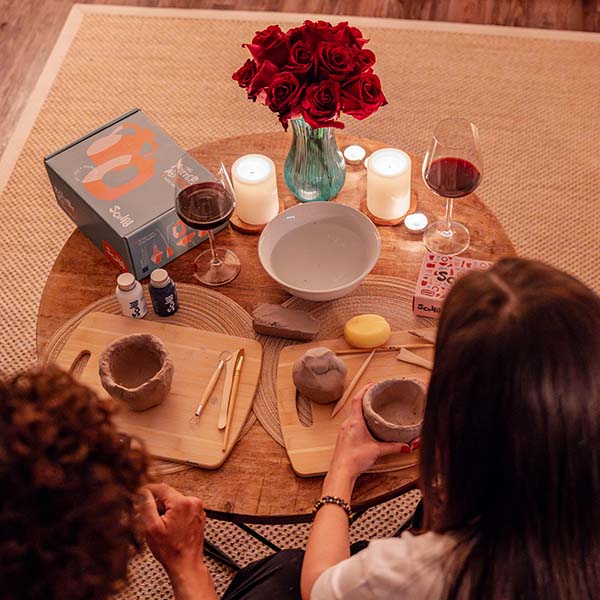 Sculpd Pottery Kit laid out on a table with roses, candles and red wine glasses with two people hand-crafting using Sculpd Air-Dry clay