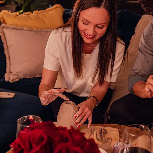 Woman shaping a Sculpd Pottery clay vase with roses and a decorative background