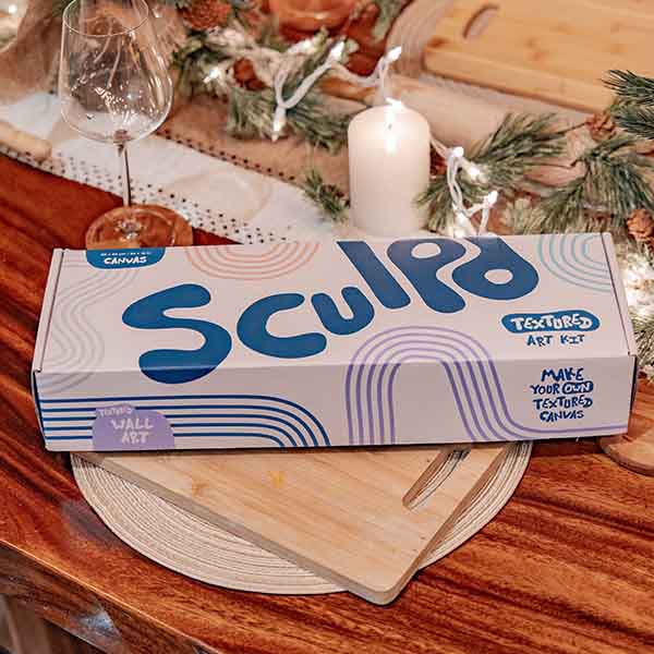 A Sculpd Textured Canvas Kit box in a cozy setup, surrounded by candles and festive greenery