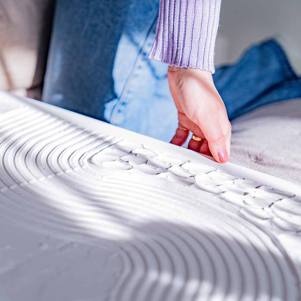 A person holding the edge of a textured canvas artwork featuring intricate, raised patterns in white made out of Sculpd Textured Canvas Kit