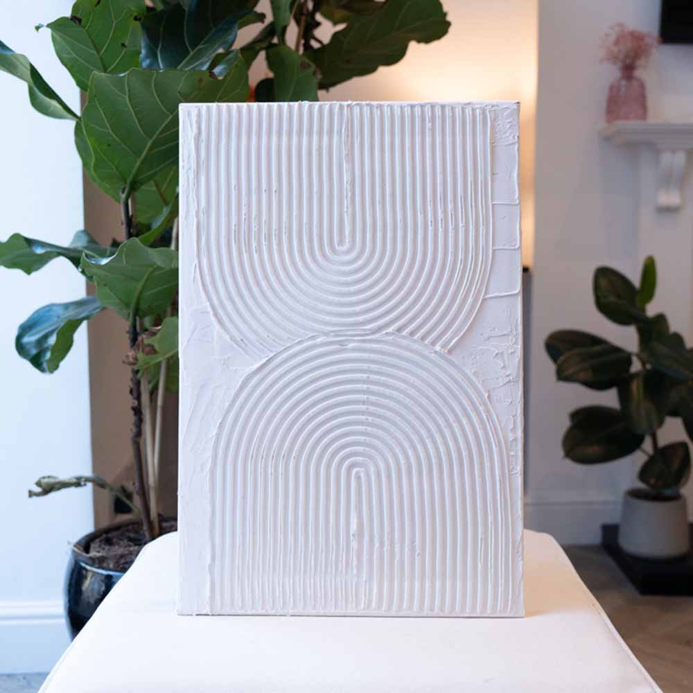 A white textured artwork with arch pattern stands on display with greenery in the background made using Sculpd Textured Canvas Kit