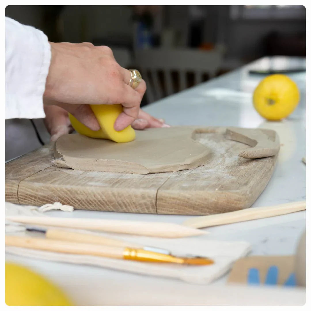 Hands demonstrating pottery techniques with Sculpd tools and clay displayed on a table
